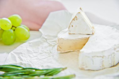 Beyaz bir kesme tahtasında fındık ile Brie peyniri, üzüm, biberiye