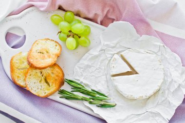 Beyaz bir kesme tahtasında fındık ile Brie peyniri, üzüm, biberiye