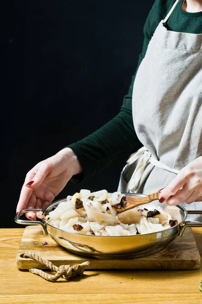 The chef cooks squid in a pan. Black background, side view, kitc