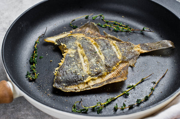 Fried flounder in a pan. Gray background, top view.