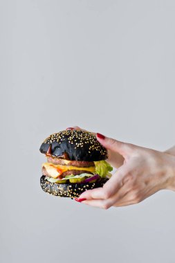 Ellerin sulu bir burger tutuyor. Yan görünüm, gri arka plan, metin alanı.