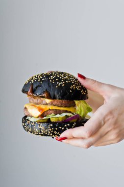 Ellerin sulu bir burger tutuyor. Yan görünüm, gri arka plan, metin alanı.