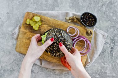 Kızın eli siyah bir burger tutuyor. Üstteki görünüm, gri arka plan, metin alanı.