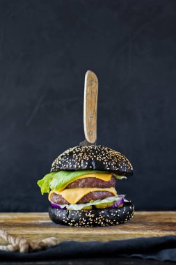 Ahşap bir tahta doğrama üzerinde siyah hamburger. Yan görünüm, siyah arka plan, metin alanı.