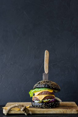 Ahşap bir tahta doğrama üzerinde siyah Burger. Yan görünüm, siyah arka plan, metin alanı.