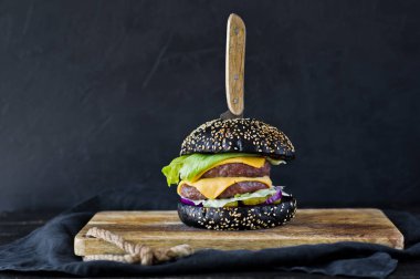 Ahşap bir tahta doğrama üzerinde siyah hamburger. Yan görünüm, siyah arka plan, metin alanı.
