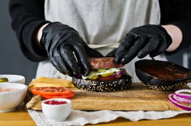 Şef cheeseburger pişiriyor. Siyah Burger pişirme kavramı. Ev yapımı hamburger tarifi. Mutfak, yan görünüm, metin alanı.