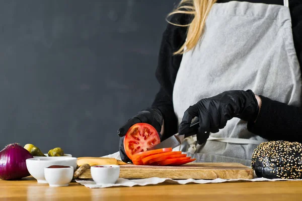 Chef cuts red tomatoes. The concept of cooking a black Burger. Kitchen, side view, space for text.