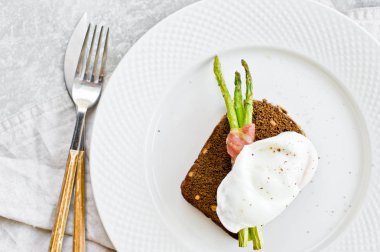Kızarmış yumurta ve pastırma içinde ızgara mini kuşkonmamış ile tost. Gri arka plan, üst görünüm, metin alanı.