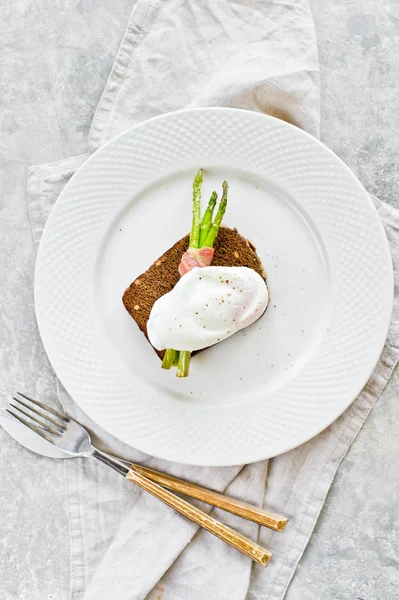 Poached egg on mini grilled asparagus in bacon. Gray background, top view, space for text.