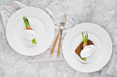 Domuz pastırması sarılmış kavrulmuş kuşkonmamış bir yumurta ile iki tabak. Gri arka plan, üst görünüm.