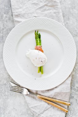 Domuz pastırması sarılmış kavrulmuş kuşkonmamış üzerinde kızartılmış yumurta. 