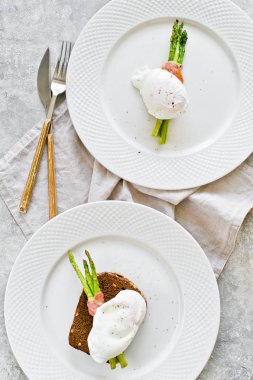 Domuz pastırması sarılmış kavrulmuş kuşkonmamış bir yumurta ile iki tabak. Gri arka plan, üst görünüm.