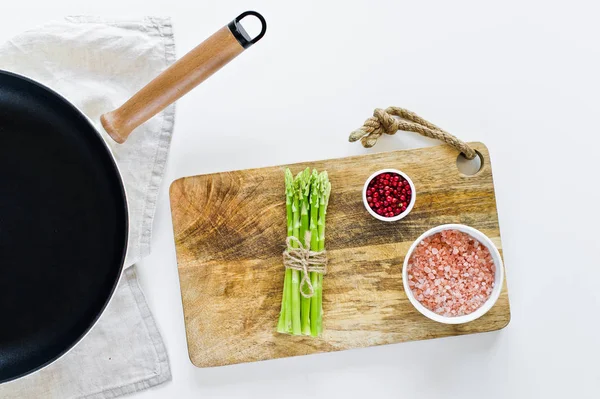 Un mazzo di mini asparagi su un tagliere di legno. Sfondo bianco, vista dall'alto, spazio per testo . — Foto Stock