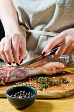 Şef, ahşap bir doğrama tahtasında çiğ kuzu bacağı pişiriyor. Biberiye, keklik, karabiber. Siyah arka plan, üst görünüm, metin alanı