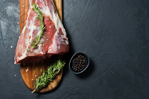 Ahşap bir tahta doğrama üzerinde kuzu ham bacak. Biberiye, keklik, karabiber. Siyah arka plan, üst görünüm