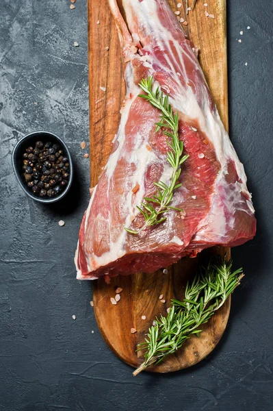 Ahşap bir tahta doğrama üzerinde kuzu ham bacak. Biberiye, keklik, karabiber. Siyah arka plan, üst görünüm