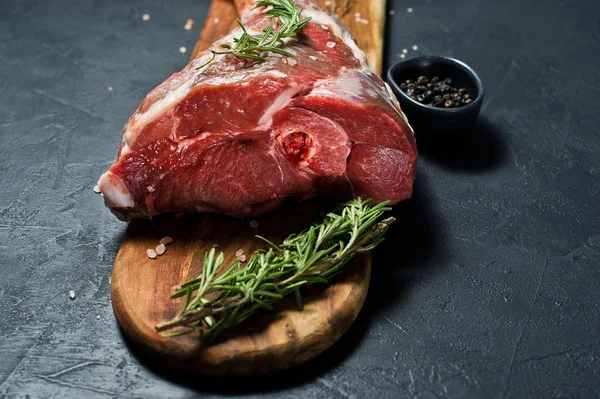 Ahşap bir tahta doğrama üzerinde kuzu çiğ bacak. Biberiye, keklik, karabiber. Siyah arka plan, yan görünüm