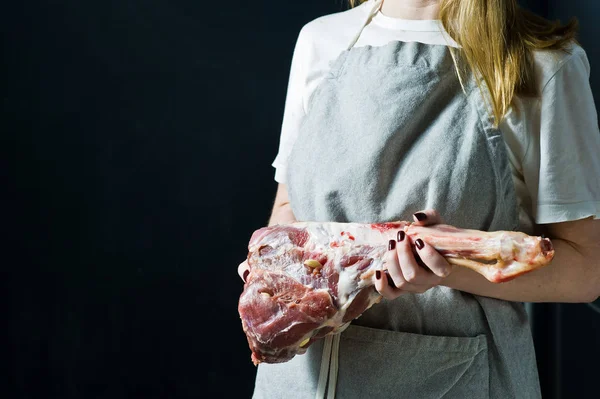 The chef is holding a raw leg of lamb. Black background, view C, space for text