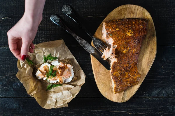 Şef, siyah ekmek ve yumuşak peynir üzerinde füme somon fileto ile bir sandviç üzerinde maydanoz Sprinkles