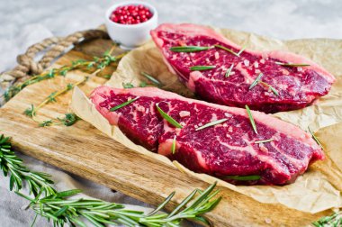 Biberiye ve pembe biber ile ahşap bir tahta doğrama üzerinde sığır sığır filetosu biftek. Gri arka plan, üst görünüm.