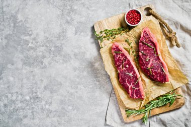 Biberiye ve pembe biber ile ahşap bir tahta doğrama üzerinde Beef rampa biftek. Gri arka plan, üst görünüm.