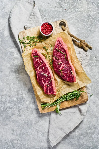 Nöt ryggbiff på trä skär bräda med rosmarin och rosépeppar. Grå bakgrund, uppifrån. — Stockfoto