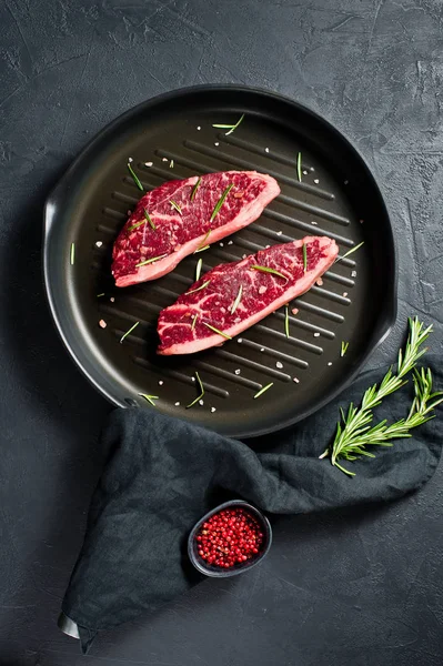 Beef sirloin steak on the grill pan. Black background, top view.