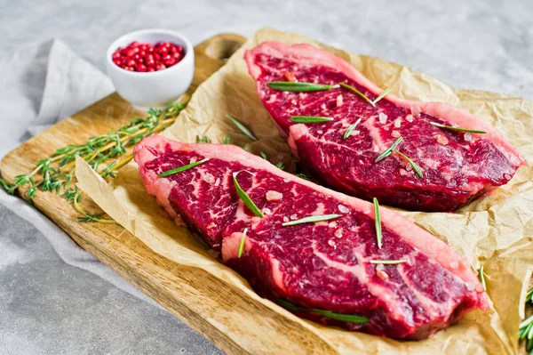 Bistecca di filetto di manzo su un tagliere di legno con rosmarino e pepe rosa. sfondo grigio, vista dall'alto . — Foto Stock