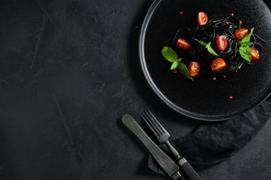 Fesleğen li siyah spagetti ve çeri domates, vejetaryen makarna. Siyah arka plan, üst görünüm, metin için alan.