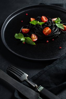 Fesleğen li siyah spagetti ve çeri domates, vejetaryen makarna. Siyah arka plan, üst görünüm, metin için alan.