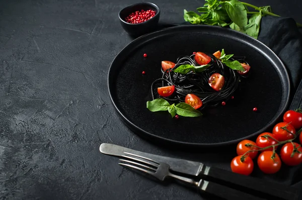 Fesleğen li siyah spagetti ve çeri domates, vejetaryen makarna. Siyah arka plan, üst görünüm, metin için alan.