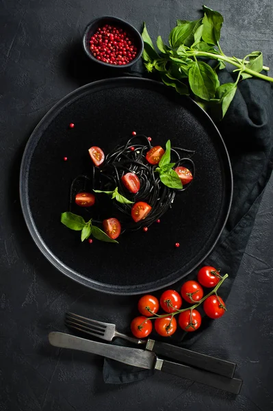 Vyvážené zdravé jídlo, černé špagety s bazalkou a třešňovou rajčaty, vegetariánské těstoviny. Černé pozadí, pohled shora, místo pro text. — Stock fotografie