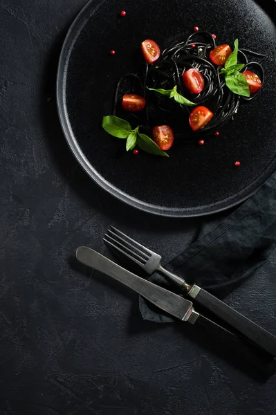 Prato vegetariano, espaguete preto com manjericão e tomate cereja. Fundo preto, vista superior . — Fotografia de Stock