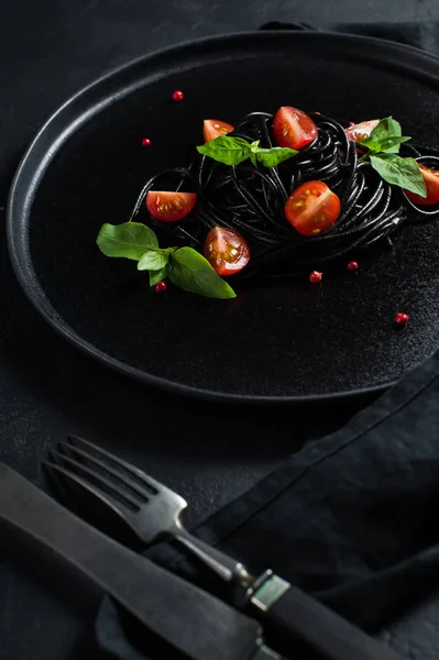 Black spaghetti with Basil and cherry tomatoes, vegetarian pasta. Black background, top view, space for text. — Stock Photo, Image