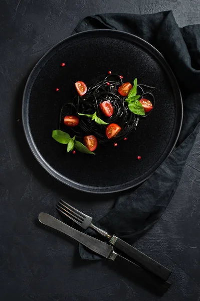 Massa vegetariana preta com manjericão e tomate cereja. Fundo preto, vista superior . — Fotografia de Stock