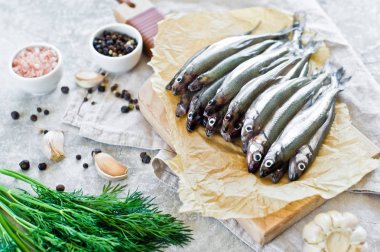 Ahşap doğrama tahtası, dereotu, pembe tuz, biber ve sarımsak üzerinde çiğ uskumru. Gri arka plan, üst görünüm, metin için alan.