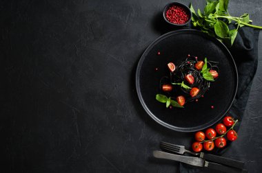 Fesleğen li siyah spagetti ve çeri domates, vejetaryen makarna. Siyah arka plan, üst görünüm, metin için alan.