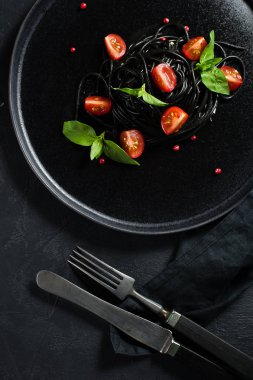 Fesleğen ve kiraz domates ile siyah vejetaryen makarna. Siyah arka plan, üst görünüm.