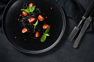 Fesleğen li siyah spagetti ve çeri domates, vejetaryen makarna. Siyah arka plan, üst görünüm, metin için alan.