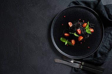 Fesleğen li siyah spagetti ve çeri domates, vejetaryen makarna. Siyah arka plan, üst görünüm, metin için alan.