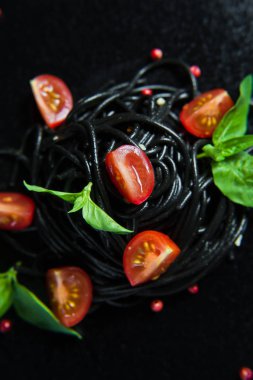 Fesleğen ve kiraz domates ile siyah vejetaryen makarna. Siyah arka plan, üst görünüm.