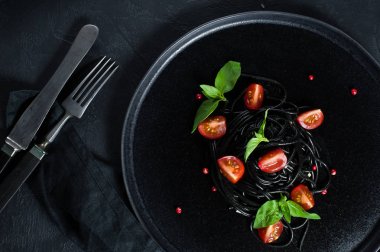 Fesleğen ve kiraz domates ile siyah vejetaryen makarna. Siyah arka plan, üst görünüm.