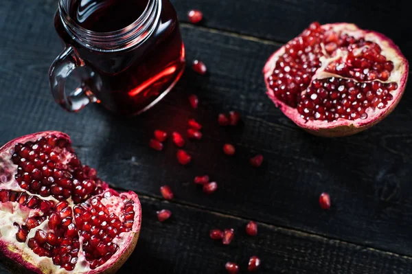 Rijpe granaatappel en een glas granaatappel sap op een zwarte houten achtergrond. — Stockfoto