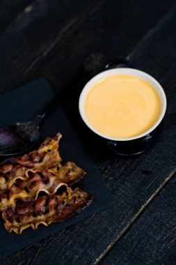 Siyah arka planda kızarmış pastırma ile kabak püresi çorbası.