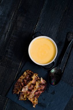 Siyah arka planda kızarmış pastırma ile kabak püresi çorbası.