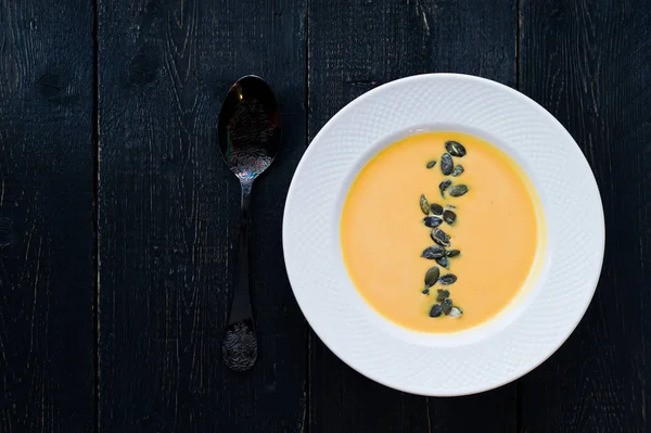 Siyah bir arka plan üzerinde beyaz bir tabakta tohumları ile kabak çorbası.