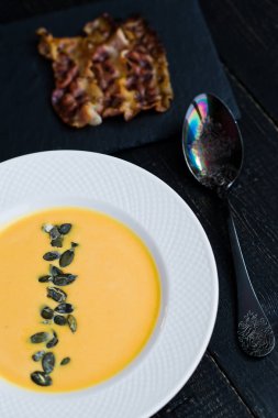 Siyah arka plan üzerinde beyaz tabakta kızarmış pastırma ile Kabak çorbası.