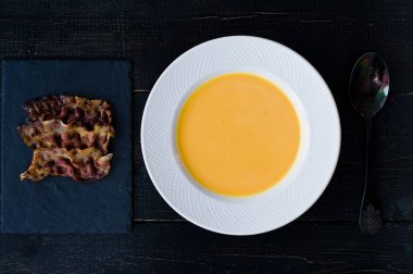 Siyah arka plan üzerinde beyaz tabakta kızarmış pastırma ile Kabak çorbası.