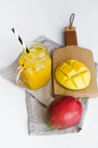 Ripe mango, half mango and a glass of mango juice with a tube on a wooden cutting Board.